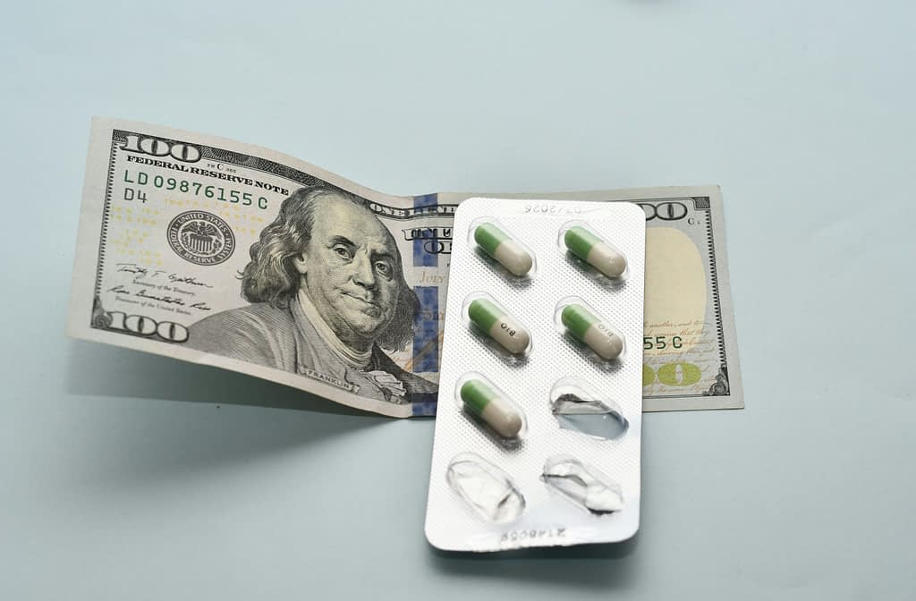 Hundred dollar bill with pharmaceutical pills blister representing Novo Nordisk investment and high drug costs