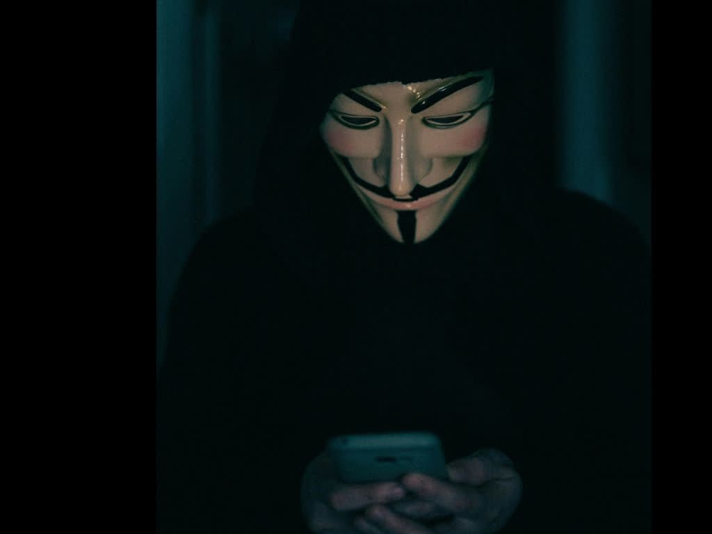 Muž provádí podvodné telefonáty z banky či od brokera. Muž je podvodník, který skrývá svou identitu a má na sobě masku.